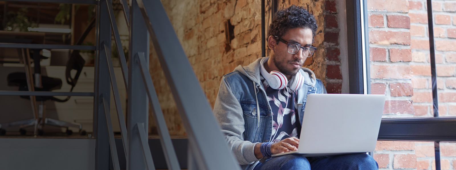 A man sits on some stairs while working on a laptop