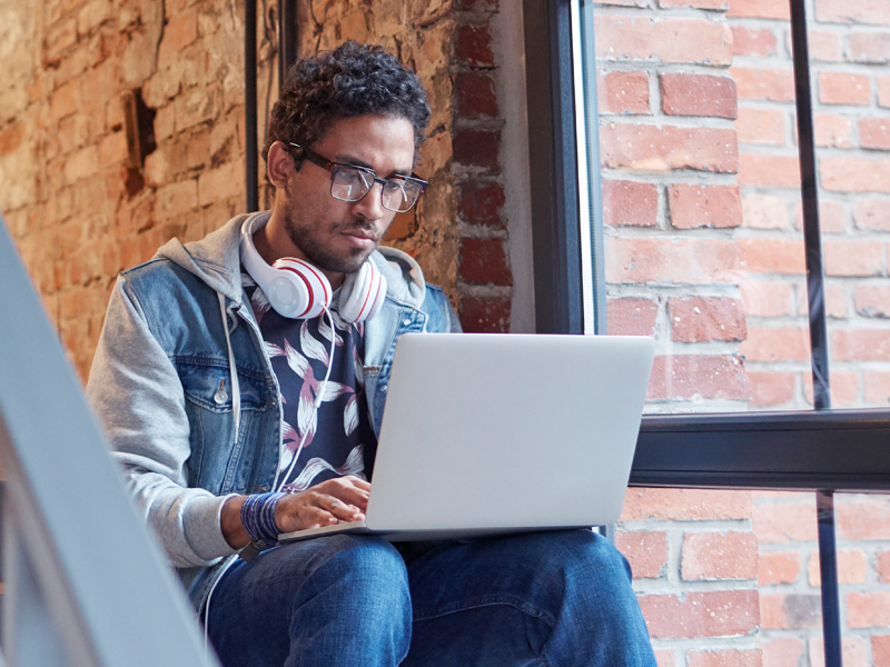 A man sits on some stairs while working on a laptop